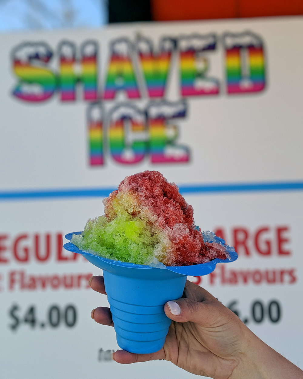 shaved ice cup is held up in front of the shaved ice menu sign